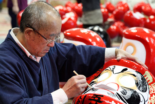 Junichi Nakata, president of the association of tumblers in Takasaki, draws eyebrows and a beard on a tumbler, Dec 14, 2010.Tumblers in Takasaki became famous because of its distinctive eyebrows and beard. [Xinhua]