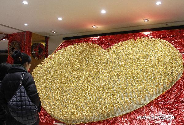 A customer looks at a heart-shaped pattern consisting of 1,999 golden roses made by foil of 99.99 percent gold at a gold store in Nanjing, capital of east China&apos;s Jiangsu Province, Dec. 15, 2010. The price of the golden rose is 299 RMB yuan (45 US dollars) per item. [Xinhua] 