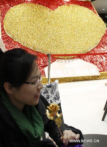 An customer holds a golden rose in front of a heart-shaped pattern consisting of 1,999 golden roses made by foil of 99.99 percent gold at a gold store in Nanjing, capital of east China&apos;s Jiangsu Province, Dec. 15, 2010. The price of the golden rose is 299 RMB yuan (45 US dollars) per item. [Xinhua] 