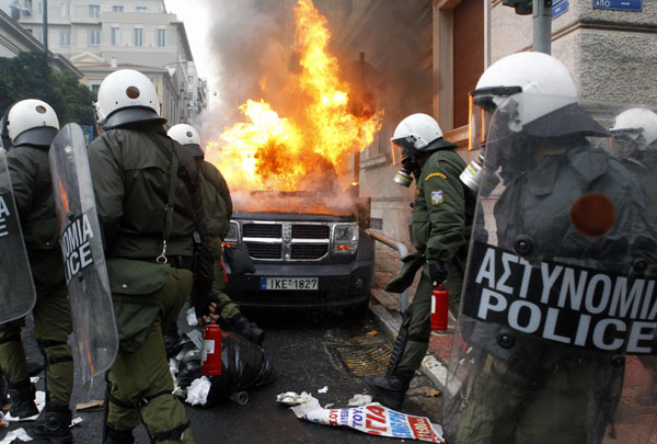 A group of riot policemen walk by a burning car caused by a petrol bomb thrown by protesters during clashes in central Athens Dec 15, 2010. [China Daily/Agencies]