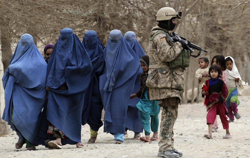 Afghan women and children walk past a German Bundeswehr army soldier from Charlie platoon of the 2nd Paratroop Company 373 during a mission in the city of Iman Sahib, north of Kunduz, northern Afghanistan, December 15, 2010. [China Daily]
