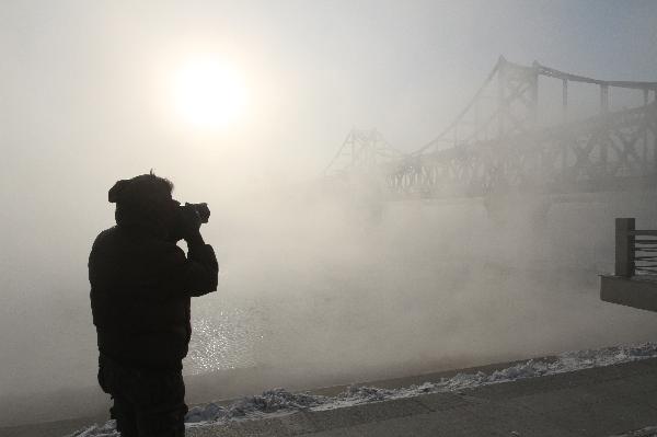 A man takes photos by the Sino-DPRK Friendship Bridge on the Yalu River which is vaguely seen in the winter fog in Dandong, a border city of northeast China&apos;s Liaoning Province, Dec. 16, 2010. [Xinhua] 
