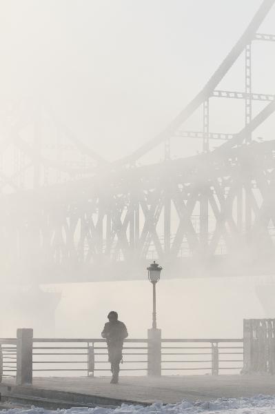 People walk by the Sino-DPRK Friendship Bridge on the Yalu River which is vaguely seen in the winter fog in Dandong, a border city of northeast China&apos;s Liaoning Province, Dec. 16, 2010. [Xinhua]