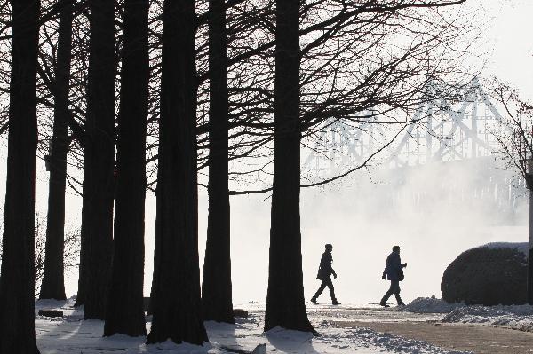 People walk by the Sino-DPRK Friendship Bridge on the Yalu River which is vaguely seen in the winter fog in Dandong, a border city of northeast China&apos;s Liaoning Province, Dec. 16, 2010.