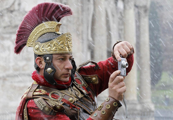 A man dressed as an ancient Roman Centurion takes a picture during a falling snow in front of Colosseum, in Rome Dec 17, 2010. [China Daily/Agencies]