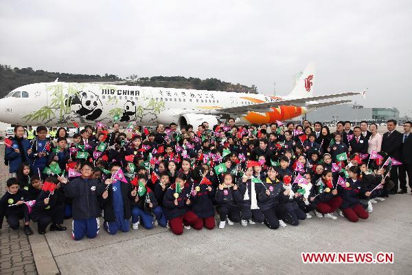 Children pose for a group photo in front of the Air China chartered plane carrying the giant pandas 'Kai Kai' and 'Xin Xin' at the airport in Macao, south China, Dec. 18, 2010. 