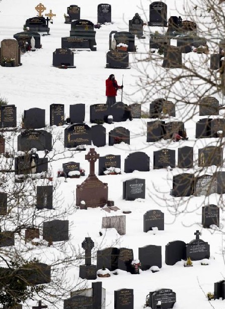 A woman says a prayer as she clears snow in St Mary&apos;s Parish church graveyard in the village of Cushendall in the Glens of Antrim , Northern Ireland Dec 19, 2010. [China Daily/Agencies] 