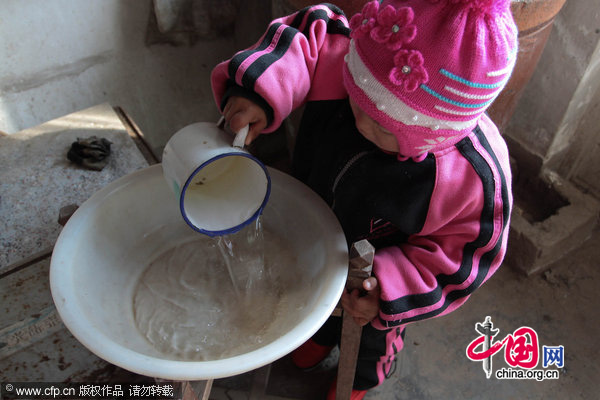 Three-year-old Dong Xinyi helps prepare water for her paralyzed father in Huangjia town of East China&apos;s Shandong province, Dec 19, 2010. Dong Jian, lost the use of his legs after a traffic accident in 2007. His wife then left him and now Dong Xinyi tries to take care of her father. [CFP]