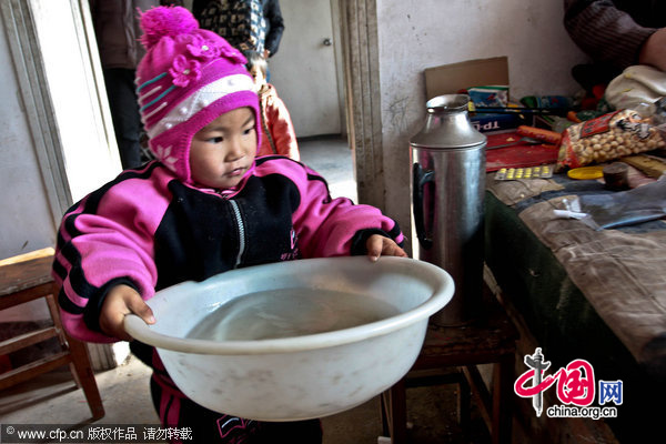 Three-year-old Dong Xinyi helps prepare water for her paralyzed father in Huangjia town of East China&apos;s Shandong province, Dec 19, 2010. Dong Jian, lost the use of his legs after a traffic accident in 2007. His wife then left him and now Dong Xinyi tries to take care of her father. [CFP]