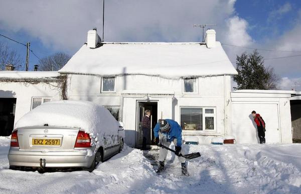 David Higgins (C) clears snow from the driveway of a house in the vilage of Martinstown in the Glens of Antrim, Northern Ireland Dec 19, 2010. The severe weather led to more disruption across Northern Ireland on Sunday, and people were advised to avoid unnecessary road journeys as snow continued to cause travel problems, local media reported.