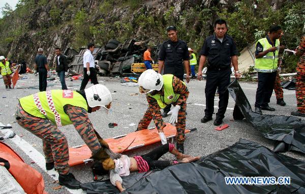 Rescue workers carry a body near the wreckage of a tour bus on a highway in Perak, a northern state in the west coast of Peninsula Malaysia, Dec. 20, 2010. A total of 27 people have been killed while 10 others injured when a tour bus hit the road divider and overturned Monday morning in Perak.[Xinhua]