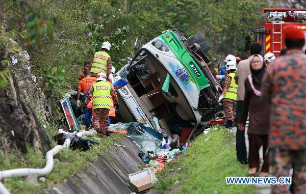 Rescue workers work near the wreckage of a tour bus on a highway in Perak, a northern state in the west coast of Peninsula Malaysia, Dec. 20, 2010. A total of 27 people have been killed while 10 others injured when a tour bus hit the road divider and overturned Monday morning in Perak.[Xinhua]