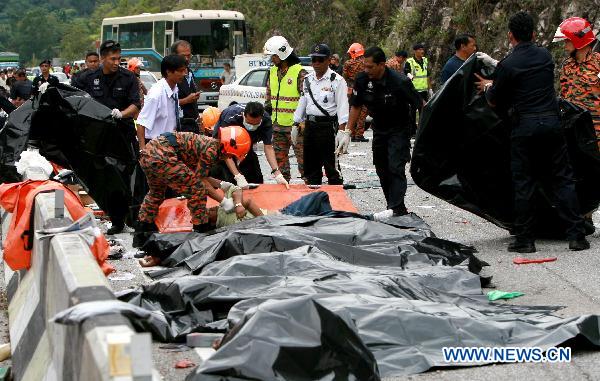 Rescue workers carry a body near the wreckage of a tour bus on a highway in Perak, a northern state in the west coast of Peninsula Malaysia, Dec. 20, 2010. A total of 27 people have been killed while 10 others injured when a tour bus hit the road divider and overturned Monday morning in Perak.[Xinhua]