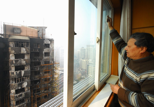 A resident living in a high-rise neighboring the fire-charred building in Shanghai cleans windows in his home on Monday. 