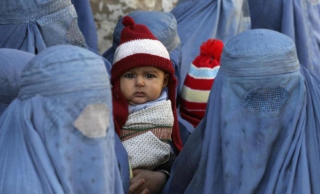 A baby boy looks on as women wait for the distribution of food by German humanitarian organization &apos;KinderBerg International&apos; to Afghan local residents in downtown Kunduz Dec 14, 2010. [China Daily/Agencies]