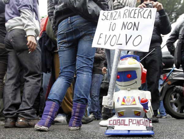 A small toy robot holds up a sign which reads, &apos;without research I can&apos;t evolve&apos;, during a demonstration in Rome Dec 22, 2010. [China Daily/Agencies]