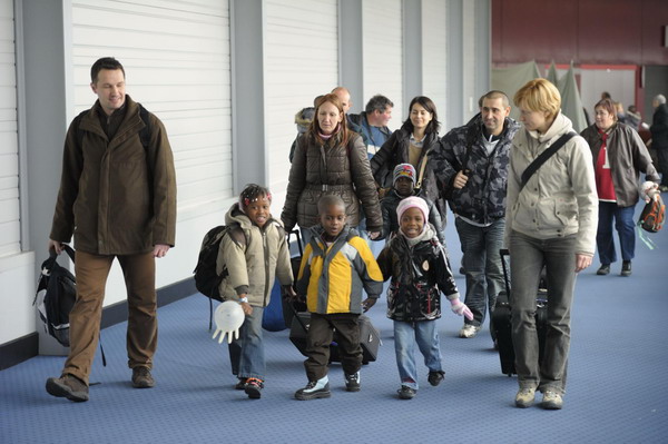 Newly-adopted children, some of the 113 orphans from Haiti, walk with their adoption families upon their arrival at the Roissy Airport, north of Paris, December 22, 2010. [China Daily/Agencies]