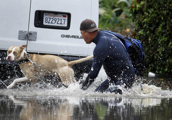 A man and his dog make their way through a flooded street after heavy rain flooded parts of San Diego, California Dec 22, 2010. [China Daily/Agencies]