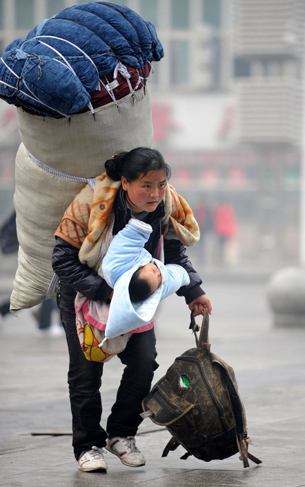 A female migrant worker is seen carrying a super big luggage and holding her baby at Nanchang railway station, southeast China&apos;s Jiangxi Province on January 30, 2010. [Xinhua]