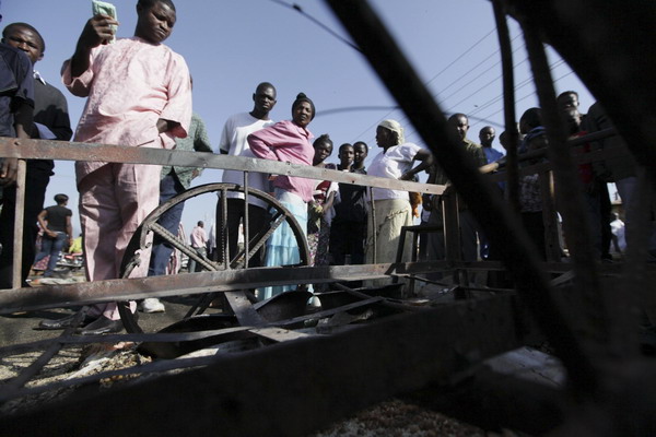 People look at the wreckage of a burnt car after an explosion in Nigeria&apos;s central city of Jos December 25, 2010. [China Daily/Agencies]