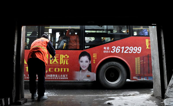 A migrant worker washes dishes at the door of his residence as a bus passes by, Dec 24, 2010. [Photo/Xinhua]