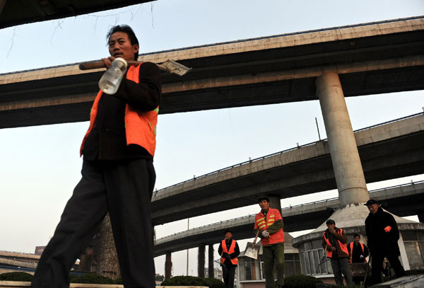 A migrant worker washes dishes at the door of his residence as a bus passes by, Dec 24, 2010. [Photo/Xinhua]