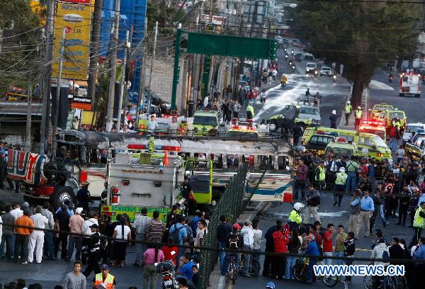 Policemen, firefighters, members of the press and pedestrians gather around a charred bus in Guatemala City, Guatemala&apos;s capital, on Jan. 3, 2011. Authorities informed that at least 5 people traveling on the bus were burned to death, and 16 others suffered severe burns after a bomb thrown by an unidentified person hit the vehicle. [Xinhua]