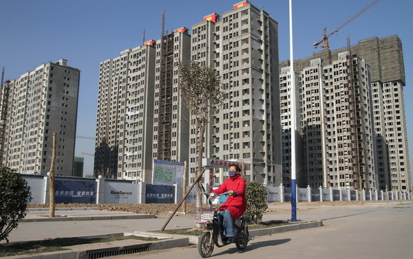 A resident rides past a development of new residential buildings on Dec 26 in Handan, Hebei province. An online survey on people's concerns found that housing ranks high on their list of priorities for the New Year. [Photo/Xinhua]