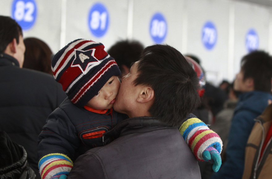 A man with a baby in his arms waits in the line to buy train tickets in Shanghai, east China, Jan. 9, 2011. Shanghai Railway Station started to sell tickets for the 2011 Spring Festival travel on Sunday. The Spring Festival travel will start on Jan. 19. [Xinhua]