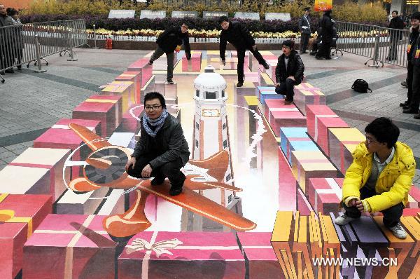 Citizens stand on a 3D painting for photo on a street in southwest China&apos;s Chongqing Municipality, Jan. 8, 2011. According to the designer, it took 26 days to finish the 3D painting which covers an area of nearly 90 square meters. [Xinhua]