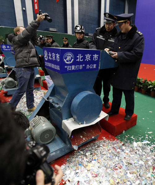 Journalists take photos as officials destroy pirated DVDs during a campaign against the production and distribution of porn and pirated publications, at a photo opportunity inside a gymnasium in Beijing Jan 10, 2011. [Photo/Agencies] 