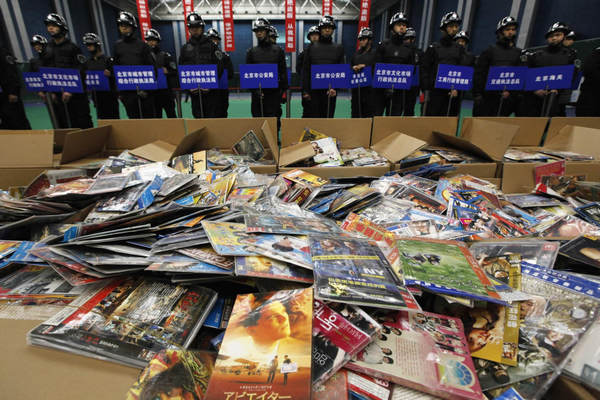 Security guards stand next to pirated DVDs which will be destroyed during a campaign against the production and distribution of porn and pirated publications, at a photo opportunity inside a gymnasium in Beijing Jan 10, 2011. [Photo/Agencies]