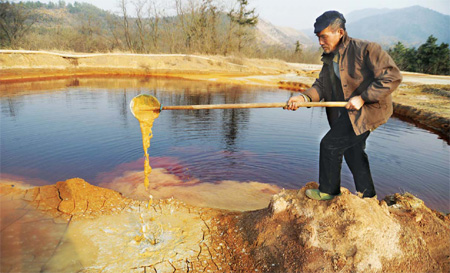A villager tries to scoop out polluted water from a pond in Xiaowang village in Anhui province on Dec 21, 2010. This pond has been heavily polluted by a nearby ore treatment plant, which produces raw materials for fertilizer. The contaminated water contains sulfur dioxide and flows directly to the fields, causing great danger to crops and various sources of drinking water. [China Daily] 