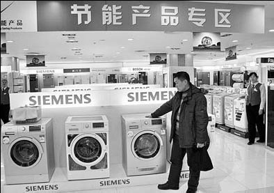 A man inspects energy-efficient washing machines at an electronics store in Beijing. [China Daily] 