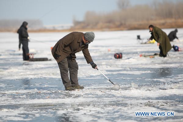 A contestant takes off floating ice from a fishing hole on the iced Waijia River duirng a fishing contest in Yantai, east China&apos;s Shandong Province, Jan. 12, 2011. More than 50 fishing fans attended the contest on Wednesday. [Xinhua]