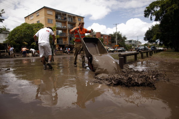 Volunteers tip barrow loads of mud from riverfront houses into the Brisbane River after floodwaters receded in the suburb of Westend January 14, 2011. [China Daily/Agemcies]