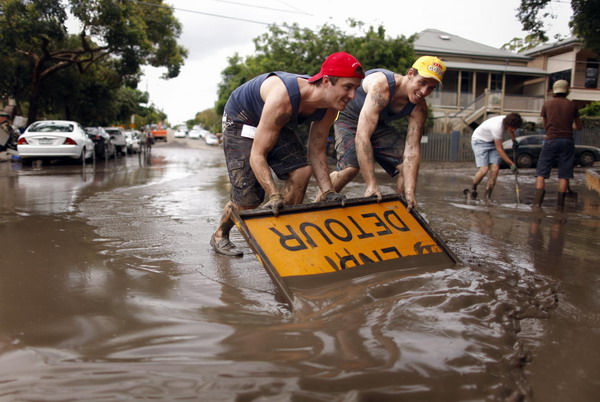 Men use a road sign to push mud off a road after floodwaters receded in the Brisbane suburb of Westend January 14, 2011. [China Daily/Agemcies] 