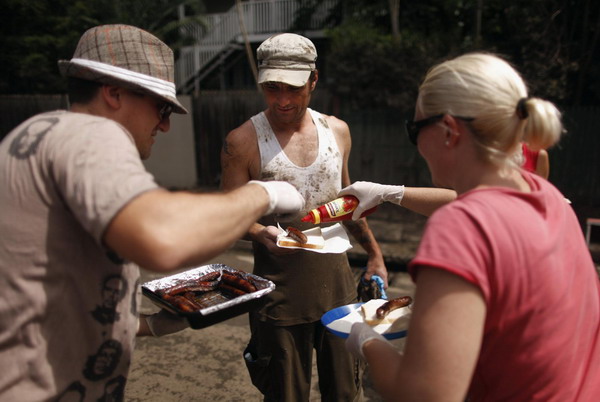 John Gamvros (L) and Claire Barlow (R) hand out a free sausage sandwich to a man cleaning a damaged house after flood waters receded in the Brisbane suburb of Westend January 14, 2011. [China Daily/Agemcies]