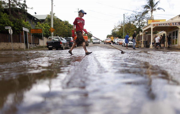 A boy pushes a broom across a mud-covered street after flood waters receded in the Brisbane River side suburb of Westend January 14, 2011. [China Daily/Agemcies]