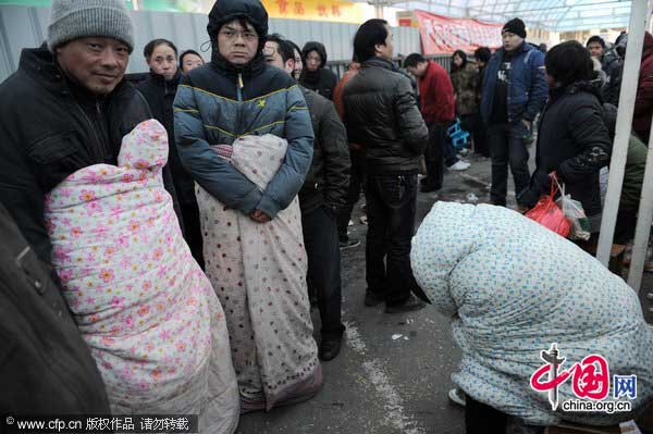 Three migrant workers bundled up in quilts wait in line to buy train tickets at a station in Hangzhou, east China&apos;s Zhejiang province on Jan 17, 2011. A cold snap hit the city bringing the temperature to -4 C. The tickets purchase frenzy begun in China ahead of the Spring Festival. A number of people camped out at stations to buy a ticket. [Photo/CFP]