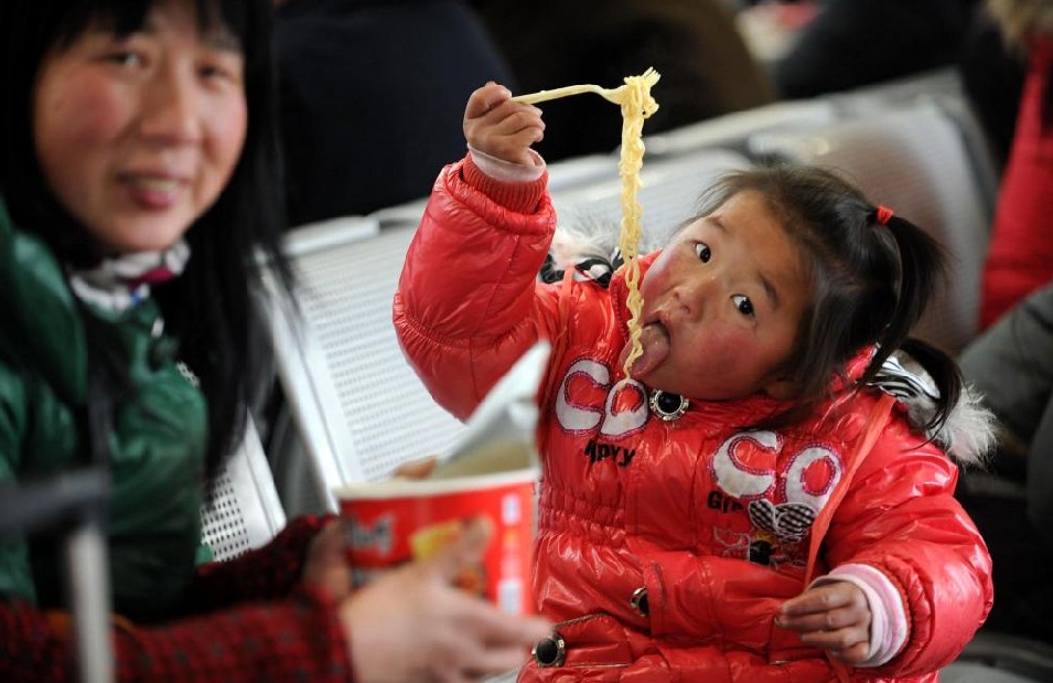 A child eats instant noodles while waiting for a train home with her mother in Hefei, Central China&apos;s Anhui province, Jan 19, 2011. [Photo/Xinhua]