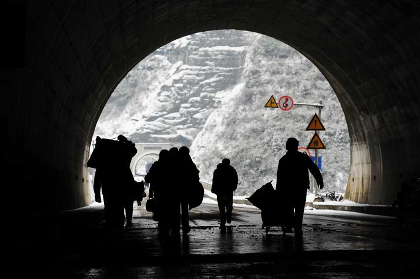 Migrant workers walk through a tunnel section of the 319 National Highway, which runs from Xiamen to Chengdu, Jan 19, 2011. The highway was closed on Wednesday due to heavy snow, forcing home-bound migrant workers to start making the final 100 kilometers of their trip on foot. They trekked 4.5 hours through snow before getting on another bus.[Photo/Xinhua]