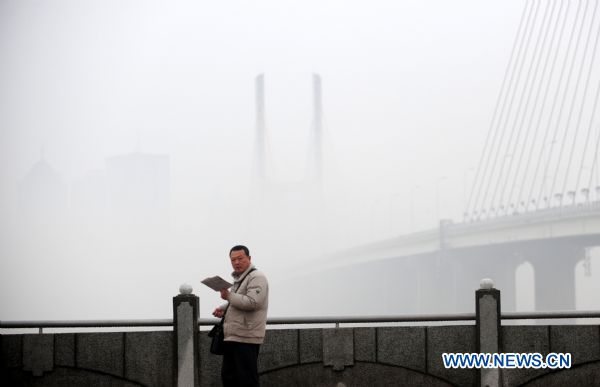 A citizen reads by the Ganjiang river in Nanchang, east China&apos;s Jiangxi province on Jan. 23, 2011. Nanchang was enveloped in fog on Sunday and the visibility in part of the city reduced to 50 meters.