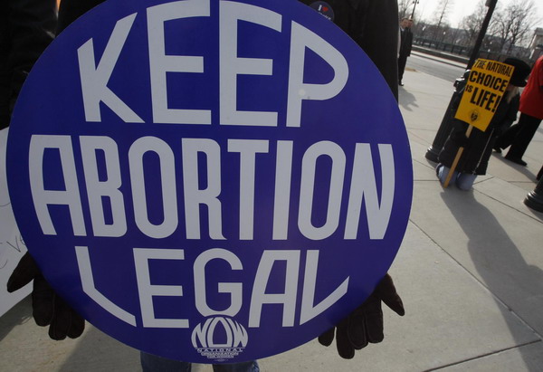 A pro-choice supporter carries a placard near a pro-life supporter (R) praying on her knees during a demonstration marking the anniversary of the Supreme Court&apos;s 1973 Roe v. Wade abortion decision in Washington, Jan 24, 2011. [China Daily/Agencies]