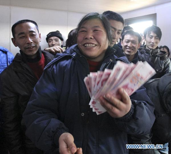 Yu Xiuchun (Front), a migrant worker, holds her salary released by a marine engineering company in Qinhuangdao, north China&apos;s Hebei Province, Jan. 24, 2010. The company released wages of January ahead of schedule for 340 migrant workers Monday, before they going back home for Chinese Spring Festival. [Xinhua]