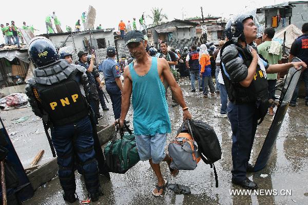 A resident carries his valuables from his home as he walks past anti-riot policemen after the demolition of shanties in San Juan City, north of Manila, Jan. 25, 2011. Some 40 people were injuried during the violent demolition that will affect more than 1,000 families in the area. [Xinhua] 