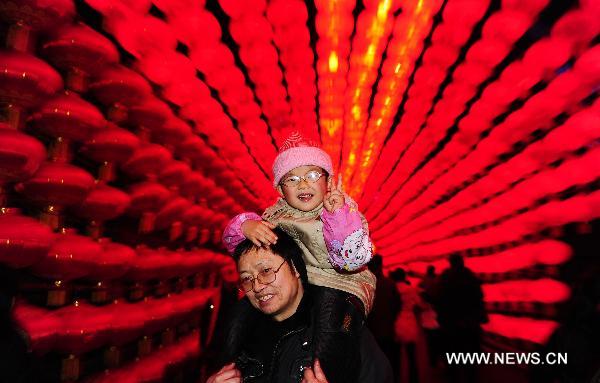 A man carrying his daughter walks through a corridor decorated with red lanterns during the 17th Zigong International Dinosaur Lantern Festival in Zigong, southwest China's Sichuan Province, Jan. 24, 2011. The lantern festival, which kicked off on Monday, will last for 43 days to celebrate the Chinese Spring Festival which falls on Feb. 3 this year. 