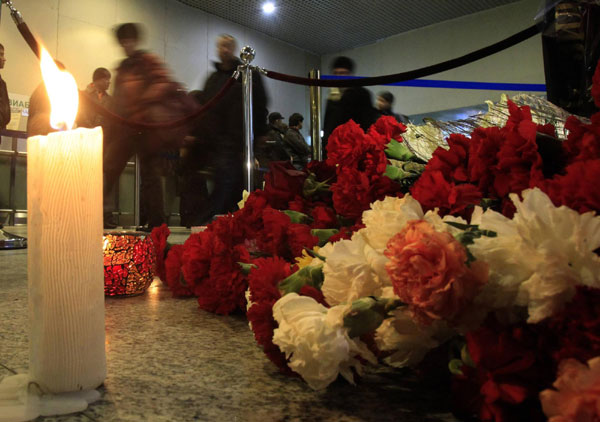 People walk past a candle and flowers left on a floor in memory of those killed in Monday&apos;s bomb explosion at Moscow&apos;s Domodedovo airport Jan 26, 2011. [China Daily/Agencies]