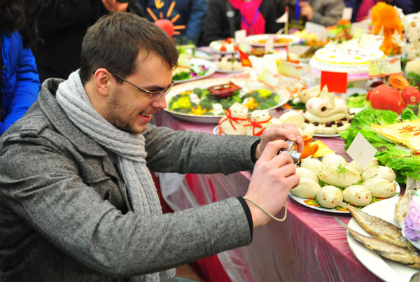 A man takes a photo of the dishes displayed on the table during a grand feast held at the Baibuting Community in Wuhan, capital of Central China&apos;s Hubei province, Jan 27, 2011. [Photo/Xinhua] 