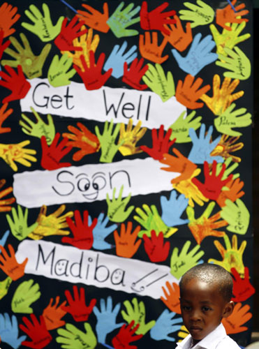 A schoolboy stands next to a placard wishing former South African president Nelson Mandela a speedy recovery outside Milpark Hospital in Johannesburg, Jan 27, 2011. [China Daily/Agencies]